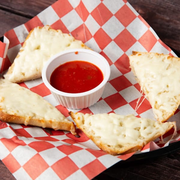 Cheesy breadsticks with melted mozzarella and a side of marinara sauce on red and white checkered paper.