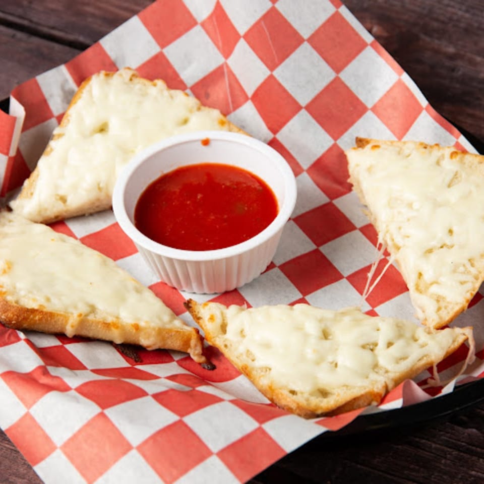 Cheesy breadsticks with melted mozzarella and a side of marinara sauce on red and white checkered paper.