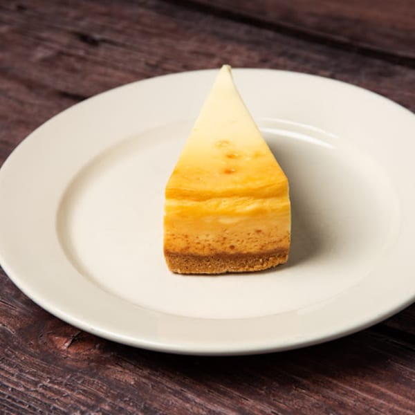 A slice of classic cheesecake with a graham cracker crust on a white plate.