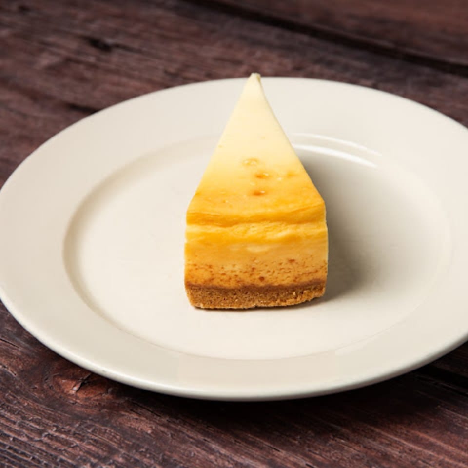 A slice of classic cheesecake with a graham cracker crust on a white plate.