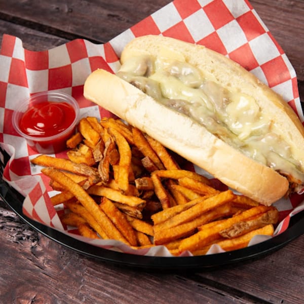 Cheesesteak sandwich with melted cheese and onions, served with a side of fries and ketchup.