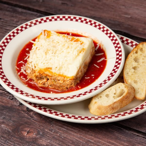 Pop's Backdoor lasagna with rich red sauce, topped with cheese, served with bread slices.